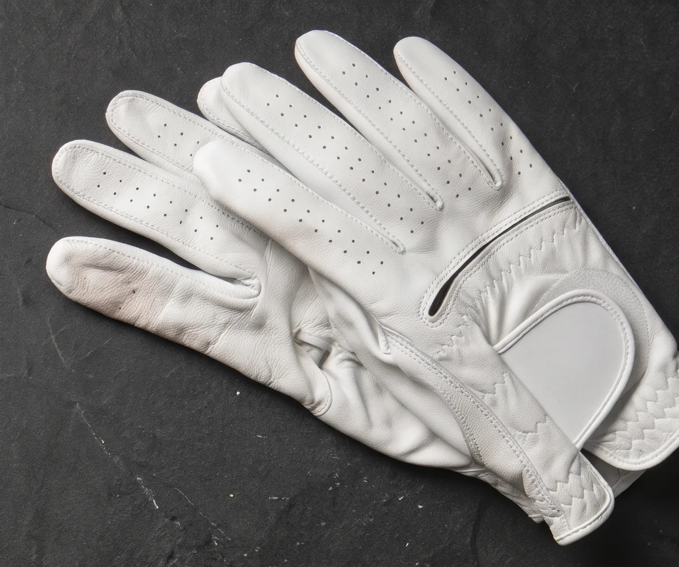White cabretta golf glove with a wrist tab and hook-and-loop strap, on dark slate